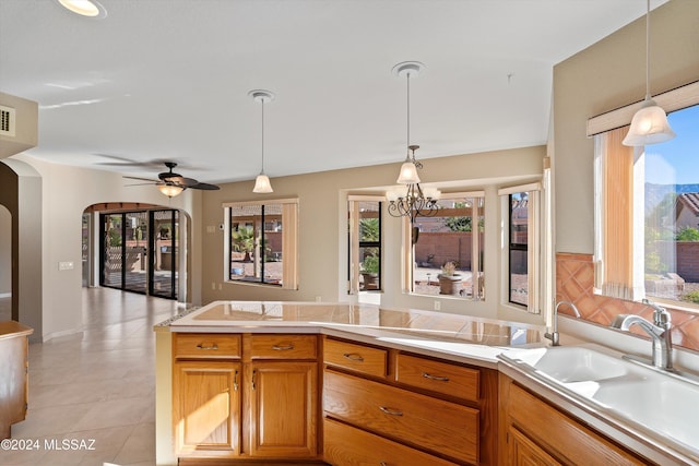 kitchen with sink, light tile patterned floors, hanging light fixtures, and ceiling fan with notable chandelier