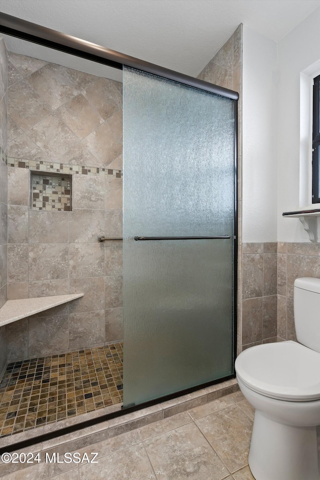 bathroom with a shower with door, tile patterned flooring, tile walls, and toilet