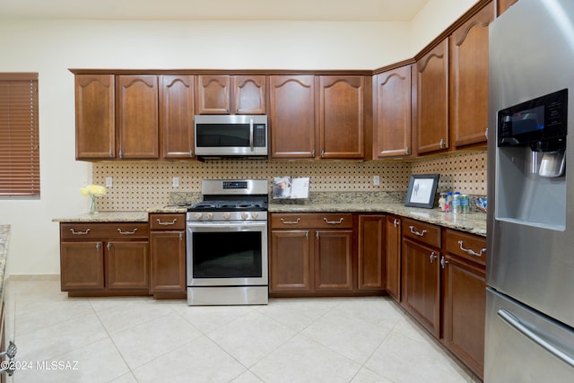 kitchen with light tile patterned floors, light stone countertops, backsplash, and appliances with stainless steel finishes