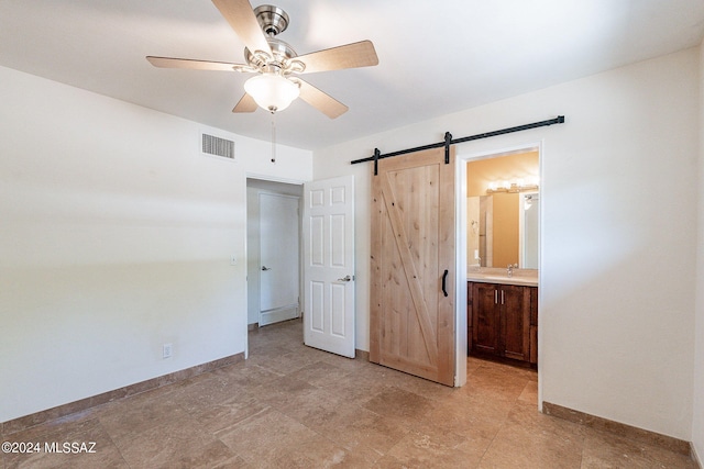 unfurnished bedroom featuring a barn door, connected bathroom, and ceiling fan