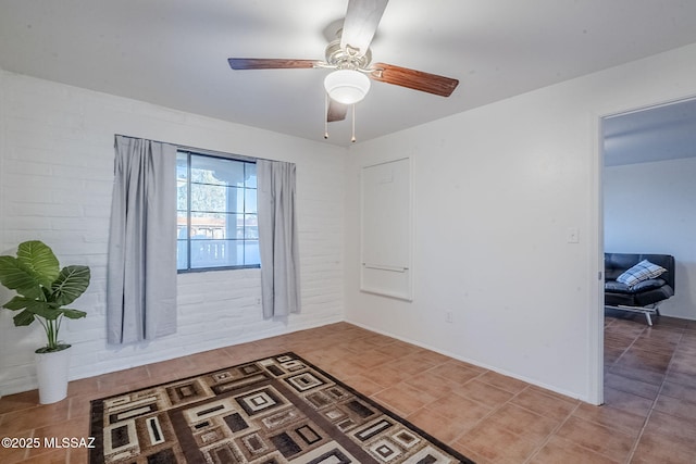 tiled empty room featuring brick wall and ceiling fan