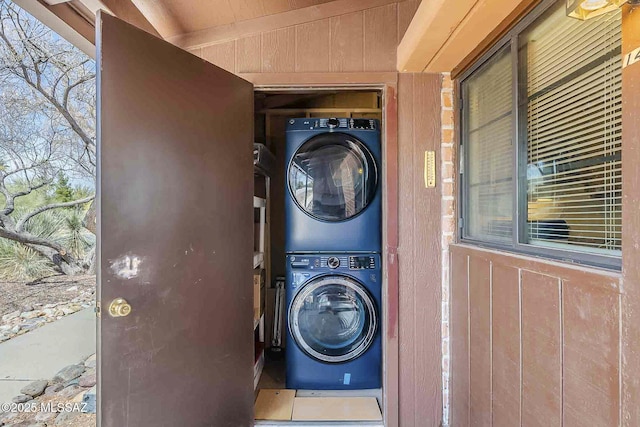 laundry area with laundry area, wooden walls, a wealth of natural light, and stacked washer / drying machine