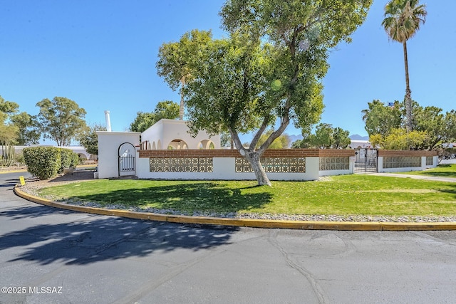 community sign with a yard, fence, and a gate