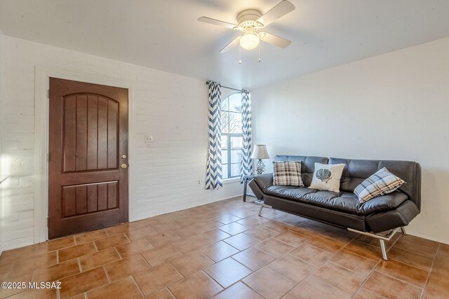 tiled living area with ceiling fan and brick wall