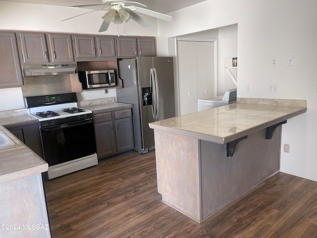 kitchen with kitchen peninsula, stainless steel appliances, a kitchen bar, dark hardwood / wood-style flooring, and ceiling fan