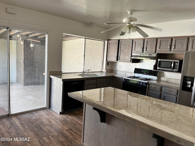 kitchen featuring sink, ceiling fan, stainless steel appliances, dark wood-type flooring, and a breakfast bar