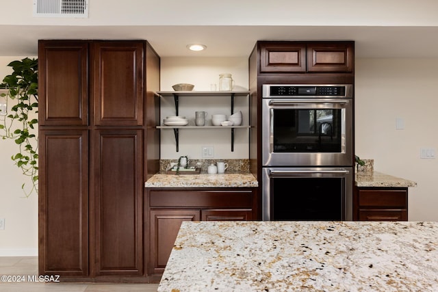 kitchen featuring stainless steel double oven, dark brown cabinetry, and light stone countertops