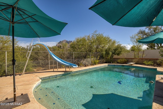 view of pool with a water slide, a diving board, and a patio area