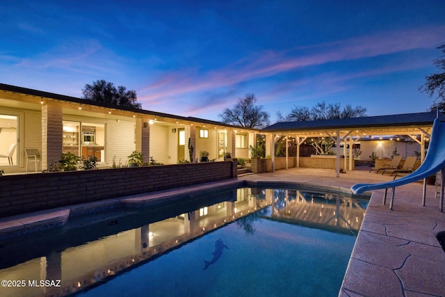 pool at dusk featuring a patio area and a water slide