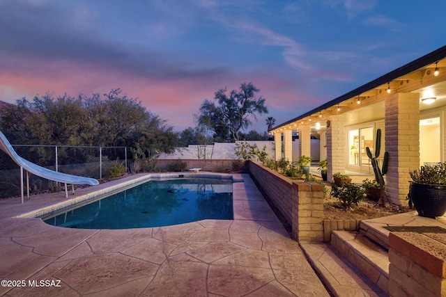 pool at dusk featuring a patio area, a diving board, and a water slide