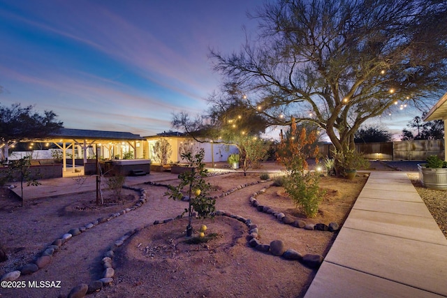 yard at dusk featuring a hot tub and a patio area