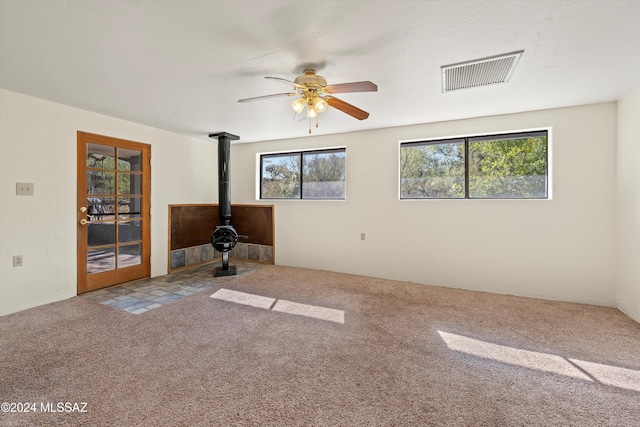 carpeted empty room featuring a wood stove and ceiling fan