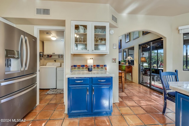 kitchen featuring blue cabinetry, stainless steel refrigerator with ice dispenser, washing machine and clothes dryer, white cabinets, and tile countertops