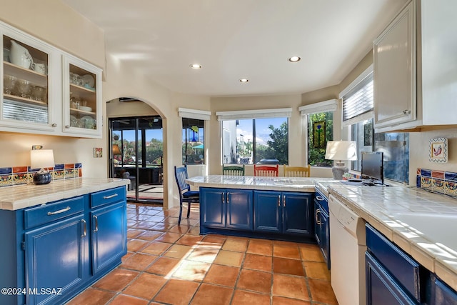 kitchen featuring blue cabinets, dishwasher, a breakfast bar area, white cabinets, and tile counters