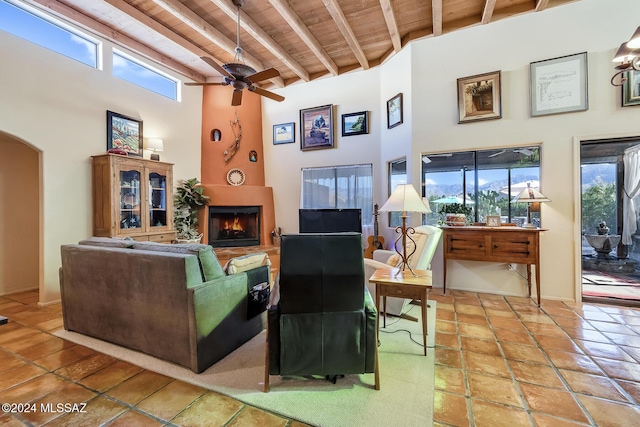 living room with wood ceiling, ceiling fan, beam ceiling, a towering ceiling, and a fireplace