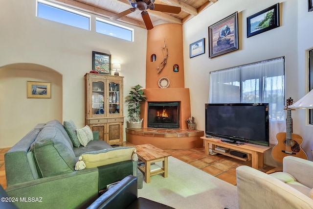 living room featuring a tile fireplace, tile patterned flooring, a high ceiling, ceiling fan, and beam ceiling