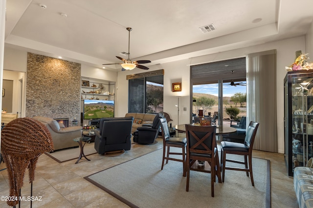 dining room featuring a fireplace, ceiling fan, and a raised ceiling