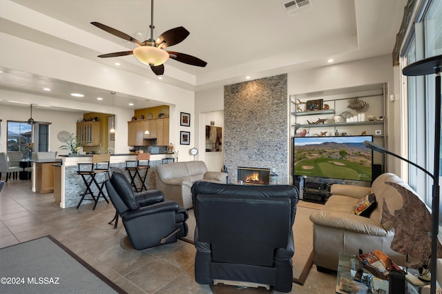 tiled living room with a fireplace, ceiling fan, and a tray ceiling