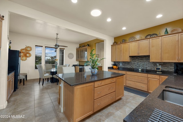 kitchen with dark stone counters, light tile patterned floors, decorative backsplash, ceiling fan, and a center island