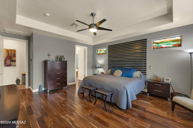 bedroom with dark hardwood / wood-style flooring, ceiling fan, and a tray ceiling