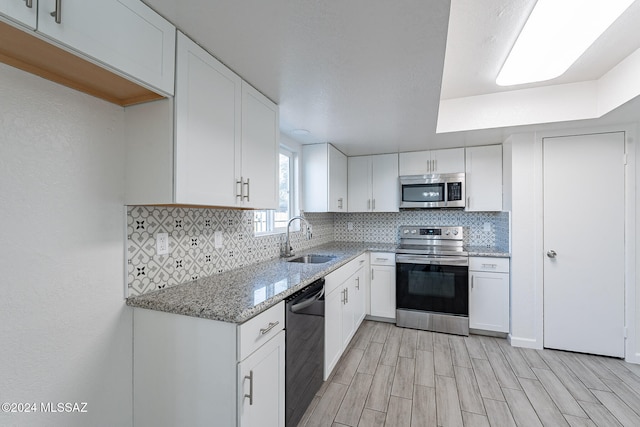 kitchen featuring white cabinetry, sink, light stone counters, appliances with stainless steel finishes, and light hardwood / wood-style flooring