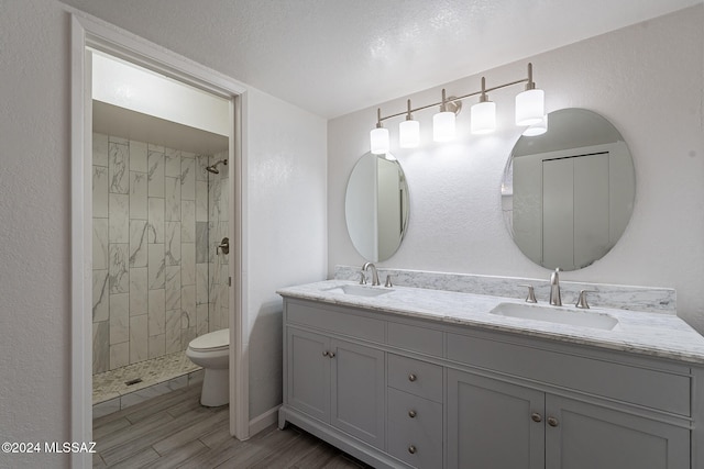 bathroom featuring wood-type flooring, tiled shower, vanity, a textured ceiling, and toilet