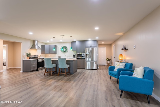 kitchen with gray cabinetry, appliances with stainless steel finishes, wall chimney range hood, and hanging light fixtures