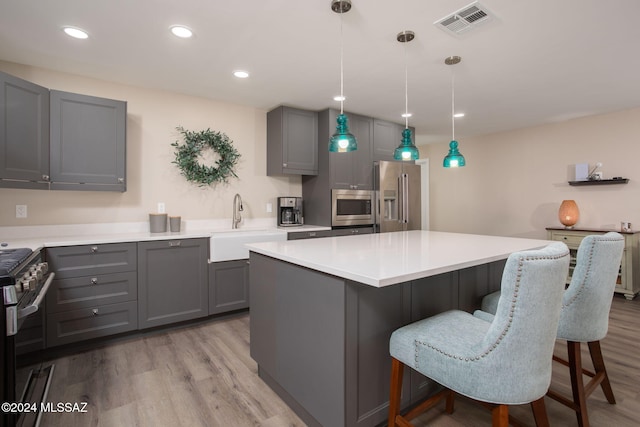 kitchen featuring a kitchen island, appliances with stainless steel finishes, light wood-type flooring, gray cabinets, and decorative light fixtures