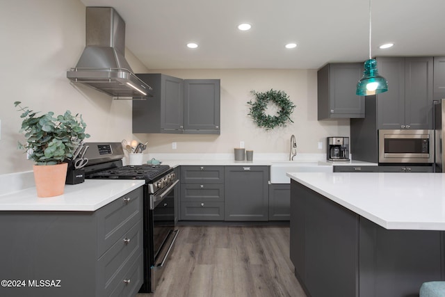 kitchen featuring wall chimney range hood, wood-type flooring, stainless steel appliances, gray cabinets, and decorative light fixtures