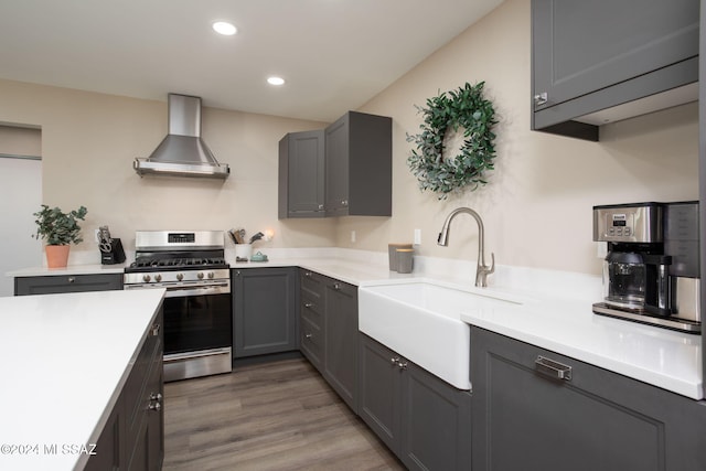 kitchen with wall chimney range hood, hardwood / wood-style flooring, gray cabinets, sink, and stainless steel gas range