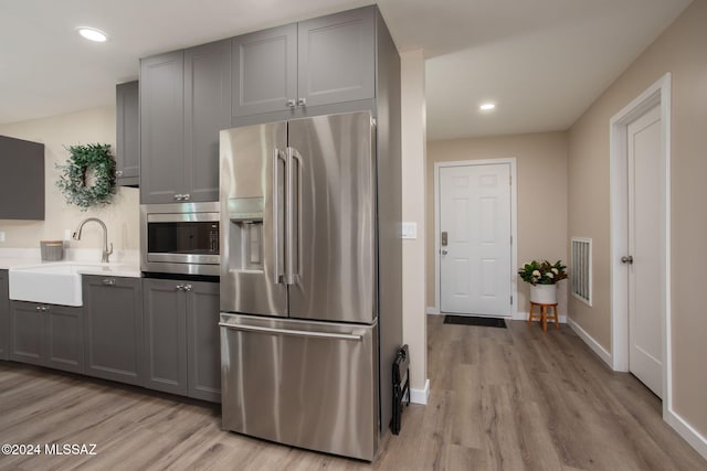 kitchen with gray cabinets, light hardwood / wood-style flooring, stainless steel appliances, and sink