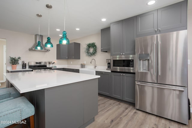 kitchen featuring wall chimney exhaust hood, gray cabinetry, pendant lighting, appliances with stainless steel finishes, and light hardwood / wood-style floors