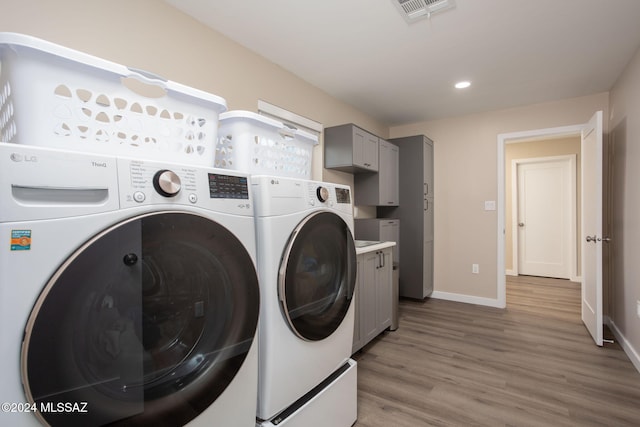 clothes washing area featuring washer and dryer, cabinets, and light hardwood / wood-style floors