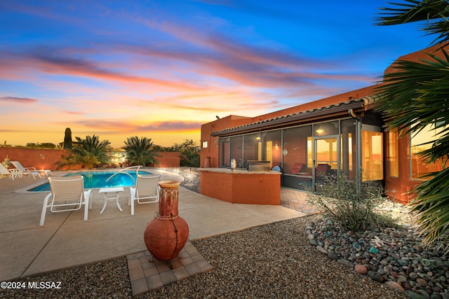 pool at dusk with a patio area and a sunroom