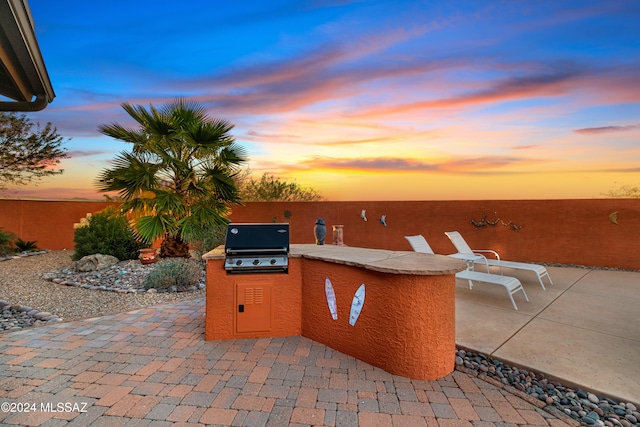 patio terrace at dusk featuring area for grilling and a grill