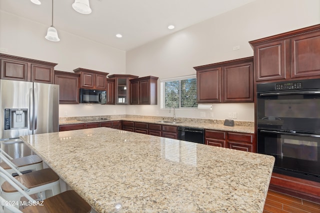 kitchen with dark hardwood / wood-style flooring, a towering ceiling, black appliances, sink, and decorative light fixtures