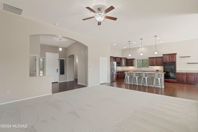 kitchen with a breakfast bar, hanging light fixtures, dark wood-type flooring, stainless steel fridge, and black double oven