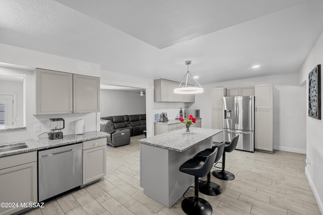 kitchen featuring a kitchen bar, a center island, hanging light fixtures, gray cabinets, and appliances with stainless steel finishes