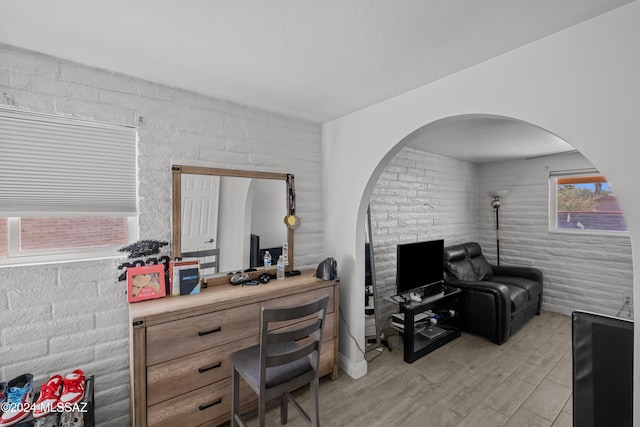 home office with a wealth of natural light, light hardwood / wood-style flooring, and brick wall