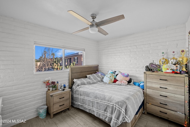 bedroom with ceiling fan, brick wall, and light wood-type flooring