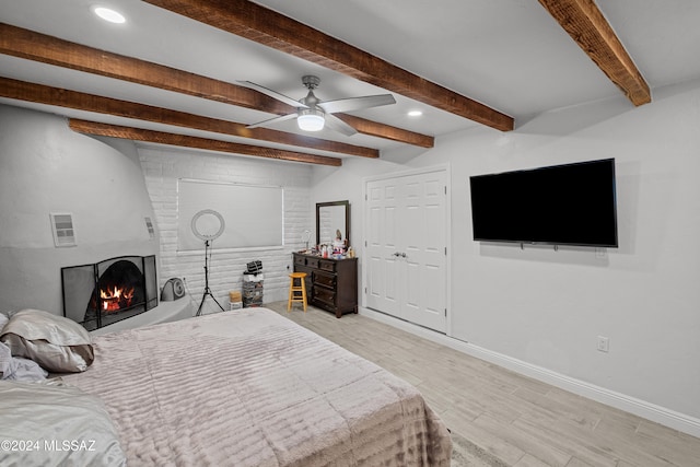 bedroom with light hardwood / wood-style floors, a large fireplace, ceiling fan, and beam ceiling