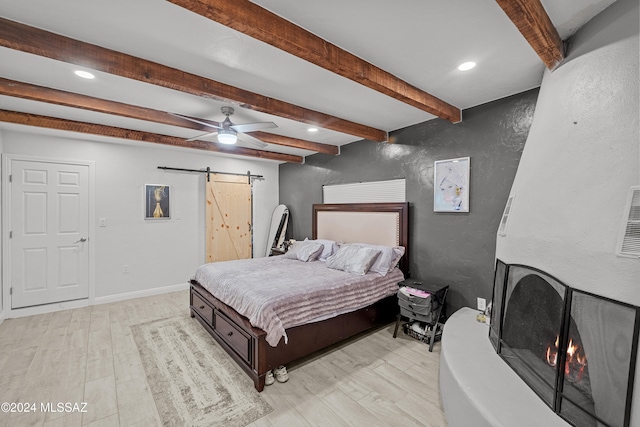 bedroom with light wood-type flooring, a barn door, ceiling fan, and beam ceiling