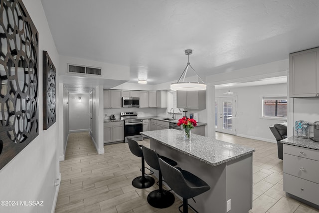 kitchen with gray cabinetry, stainless steel appliances, decorative light fixtures, sink, and a breakfast bar area