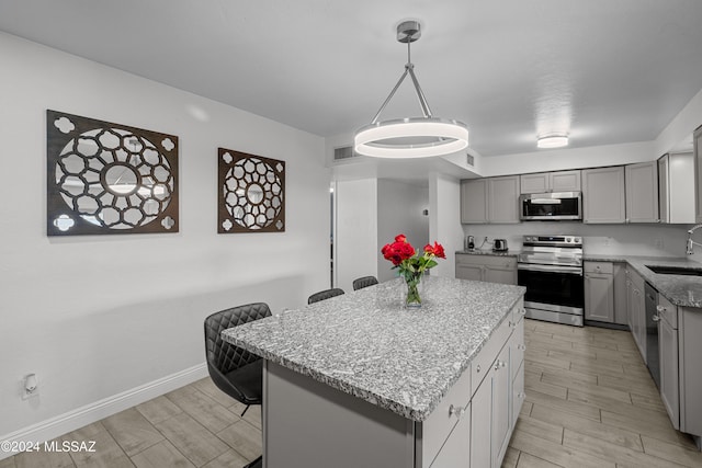 kitchen with stainless steel appliances, gray cabinets, hanging light fixtures, sink, and a center island