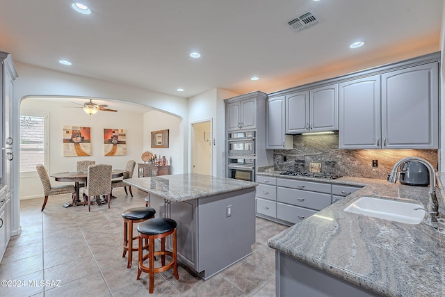 kitchen featuring light stone countertops, tasteful backsplash, ceiling fan, sink, and a kitchen island