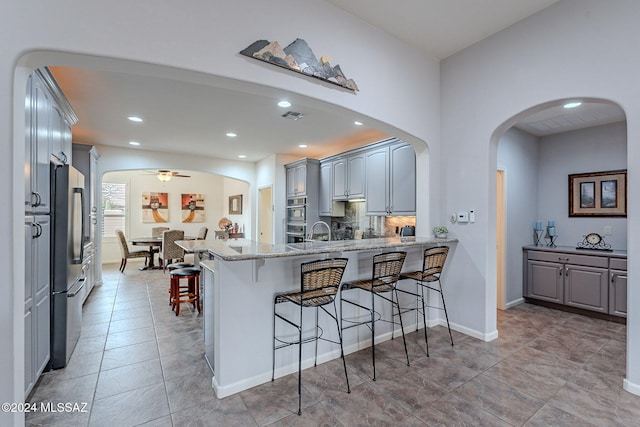 kitchen with kitchen peninsula, a kitchen breakfast bar, light stone countertops, stainless steel appliances, and gray cabinets