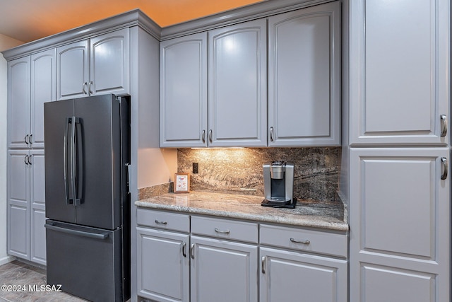 kitchen with decorative backsplash, stainless steel fridge, gray cabinets, and light stone countertops