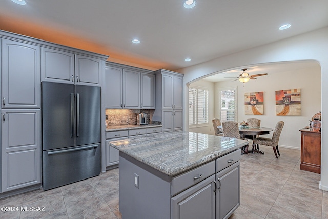 kitchen featuring gray cabinetry, a center island, backsplash, stainless steel fridge, and light stone countertops