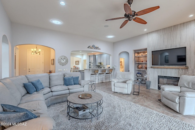 living room featuring a large fireplace, built in features, and ceiling fan with notable chandelier