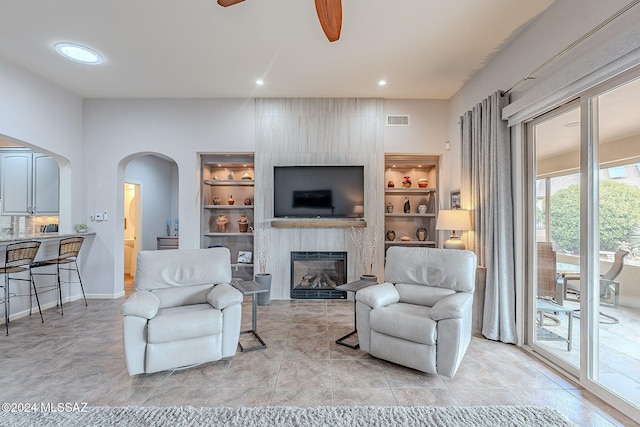 living room with built in shelves, a large fireplace, light tile patterned floors, and ceiling fan